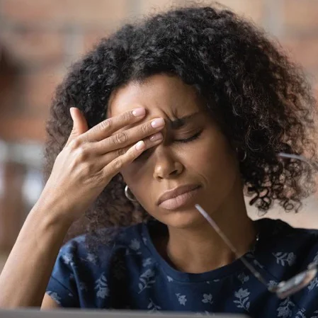 A young woman removing her glasses to rub between her eyes to relieve a headache